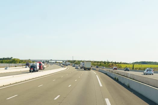 Salles-d'Aude, France - May 16, 2023: A photo of a multi-lane highway with traffic in both directions. The road is straight and curves slightly to the right. There are several vehicles, including cars, trucks, and a van.