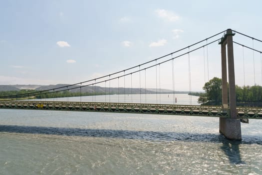 A suspension bridge spans a river, with green hills visible in the distance.