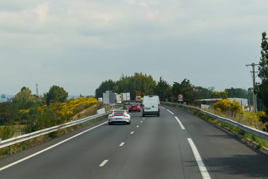 Orange, France - May 16, 2023: A white sports car drives on a highway, surrounded by lush greenery and a clear blue sky.