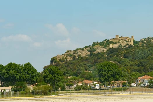 A view of a hilltop with an old castle, surrounded by green trees and shrubs, in the French countryside.