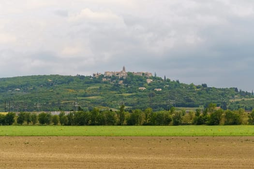 A scenic view of a hilltop village in Croatia, featuring lush green fields and a cloudy sky.
