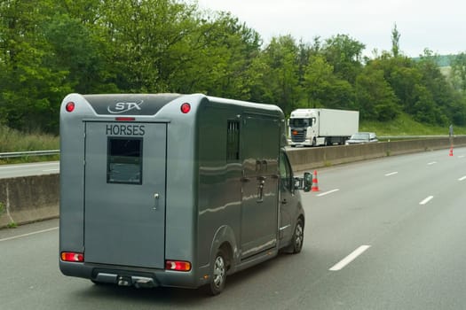 Lyon, France - May 16, 2023: A horse trailer marked with HORSES is cruising down the highway, surrounded by lush greenery beside the road.