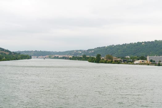 A wide shot of the Isere River flowing through the city of Grenoble, France, with a view of the surrounding mountains in the background on a cloudy day.