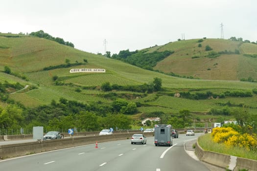 Cote-Rotie, France - May 16, 2023: Cars drive on a highway through a vineyard region with rolling hills. The sign Cote Rotie is visible on one of the hills.