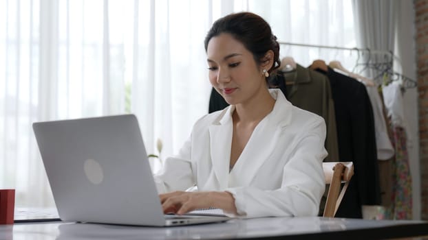 Young businesswoman sitting on the workspace desk using laptop computer for internet online content writing or remote working from home. Clothing and textile business marketing analysis. Vivancy