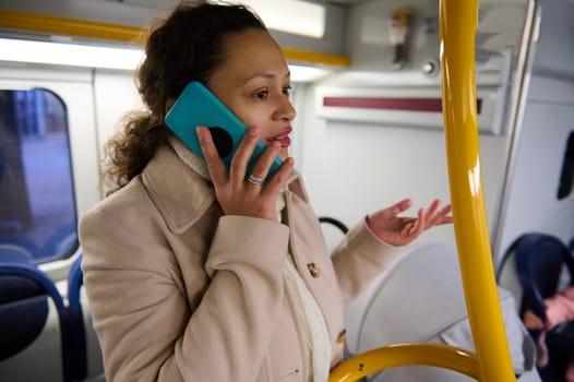 A woman speaking on her smartphone while riding a bus. She wears a winter coat and appears to be engaged in the conversation. Commuting and public transportation context.