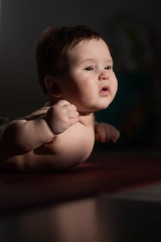 A cute little boy lies on his forearms on the floor. Vertical photo