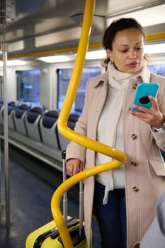 Woman standing in a train with her luggage, checking her phone while traveling. She looks engaged and focused, emphasizing travel and modern communication.