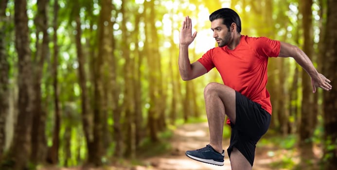 Athletic and sporty man running posture at outdoor green forest exercise session for fit physique and healthy outdoor sport lifestyle. Gaiety green foliage tree exercise workout training.