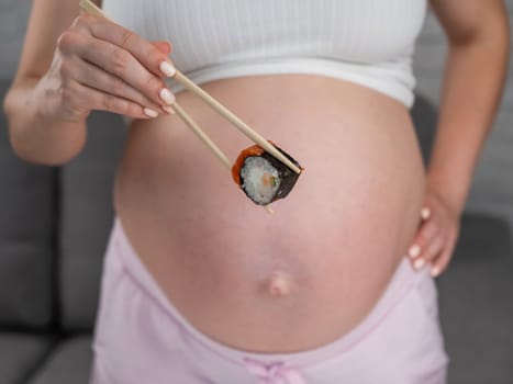 A pregnant woman holds a roll with chopsticks. Close-up of the belly