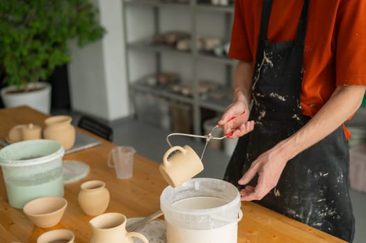 Close-up of a potter's hands glazing a ceramic mug