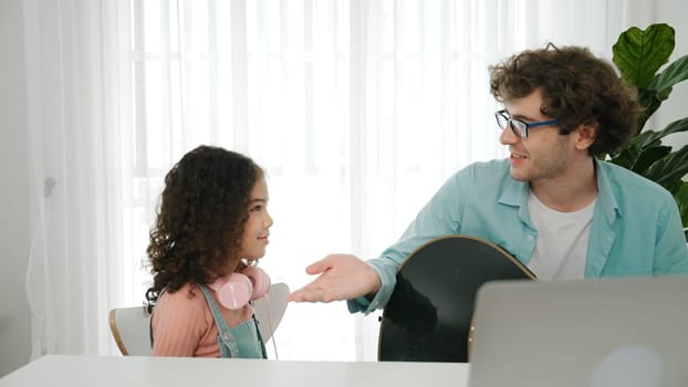 Skilled caucasian father playing guitar to relax daughter after learning engineering prompt and code. Cute schoolgirl with headphone sitting at table with laptop while listen acoustic music. Pedagogy.