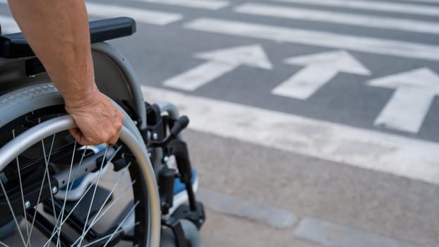 Rear view of an elderly woman in a wheelchair going to a pedestrian crossing. Close-up on wheels