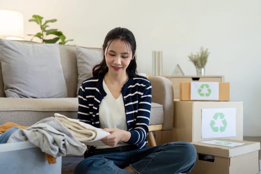 A young woman sits on the floor, sorting clothes for donation and recycling, highlighting the importance of volunteering and sustainable living.