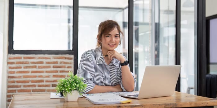 A successful businesswoman in a modern office, working on a laptop and smiling confidently. Represents professionalism, ambition, and productivity.