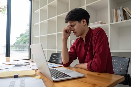 A business professional experiencing stress while working at a desk with a laptop and documents in a modern office environment.