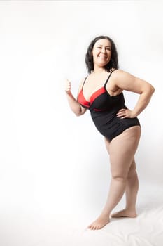 Portrait of attractive dreamy thick woman in red black swimsuit posing on white background. Body positive, photoshoot, selfie. Funny plus size model