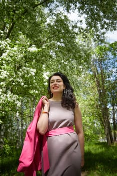 Joyous brunette woman near Blossoms of apple tree in a Spring Garden outdoors. The Concept of face and body care. The scent of perfume and tenderness