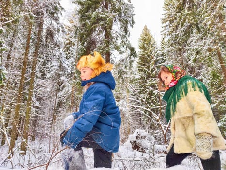 Two cute happy little cheerful children walking and having fun in winter snow forest. Photo shoot in stylized clothes of the USSR. Fur Hat with earflaps