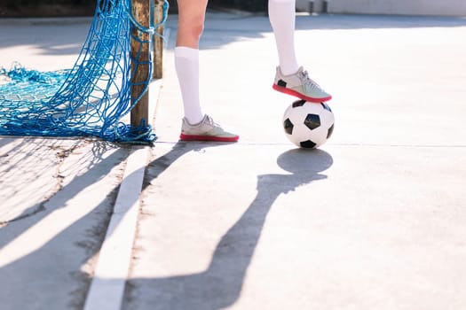close up of the feet of a female football player stepping on a soccer ball next to the goal of an urban court, concept of sport and active lifestyle, copy space for text