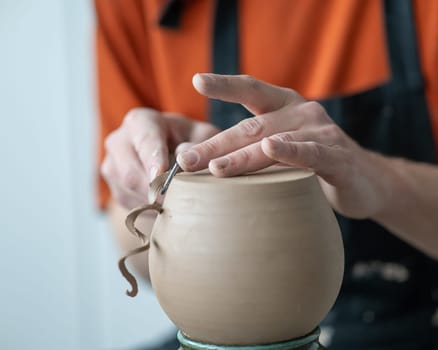 A potter works with a tool on a potter's wheel. Close-up of a man's hands