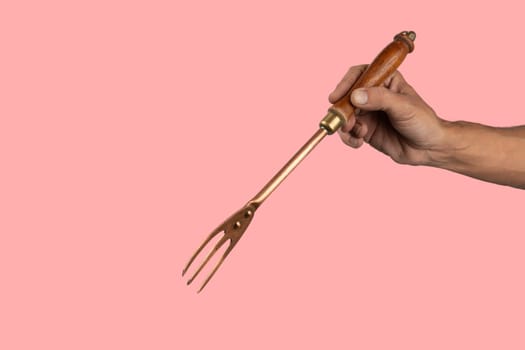 Black male hand holding a vintage brass meat fork on pink background. High quality photo