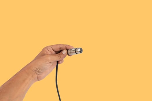 Male hand holding an XLR audio connector cable isolated on yellow background. High quality photo