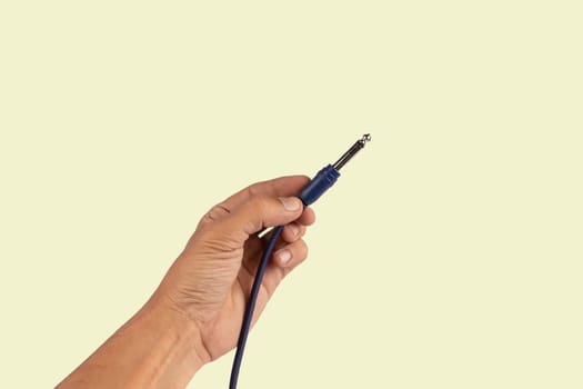 Black male hand holding an audio Jack cable isolated light green background. Guitar cable. High quality photo