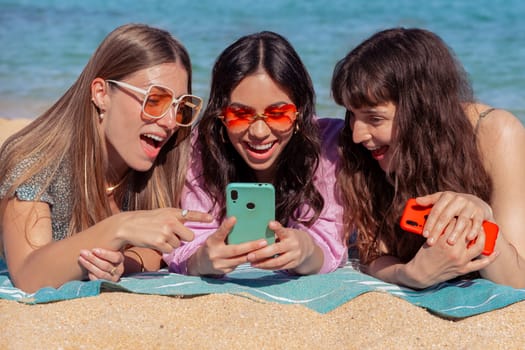 Group of smiling multiethnic women enjoying vacation. Beautiful and cheerful Gen Z girls with their mobile phones pose looking at the camera with a mobile phone.