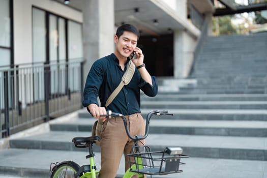 A young professional using a bicycle for eco-friendly commuting while talking on a smartphone in a modern urban environment.