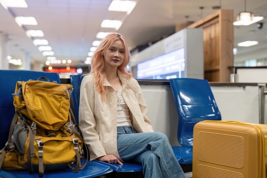 Young woman with yellow backpack and suitcase sitting in an airport terminal, ready for travel.