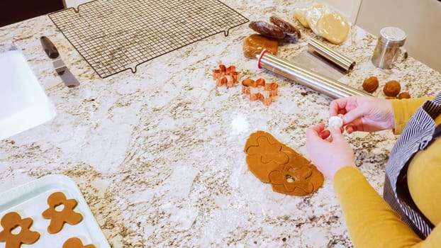 Using various festive cookie cutters, we're cutting out charming gingerbread cookies from the rolled dough on the sleek marble counter, bringing holiday cheer to the modern kitchen.