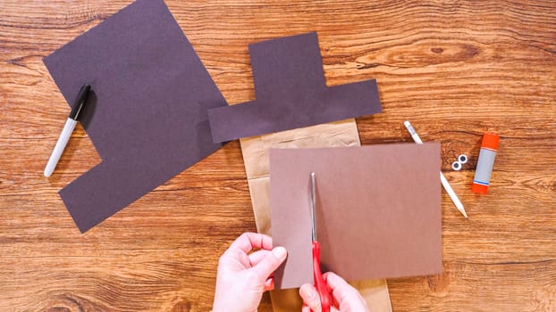 Step by step. Flat lay. Teacher guides online class through making a paper puppet from a brown bag, creatively using a wooden surface as a workspace.