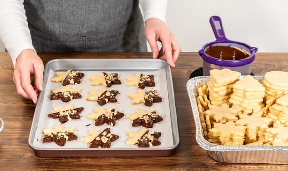 Creating cutout sugar cookies, partially dipped in chocolate and topped with hazelnut pieces, placed on parchment paper.