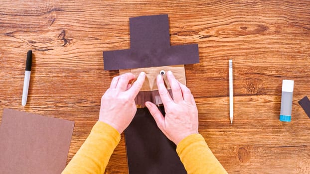 Step by step. Flat lay. Teacher guides online class through making a paper puppet from a brown bag, creatively using a wooden surface as a workspace.