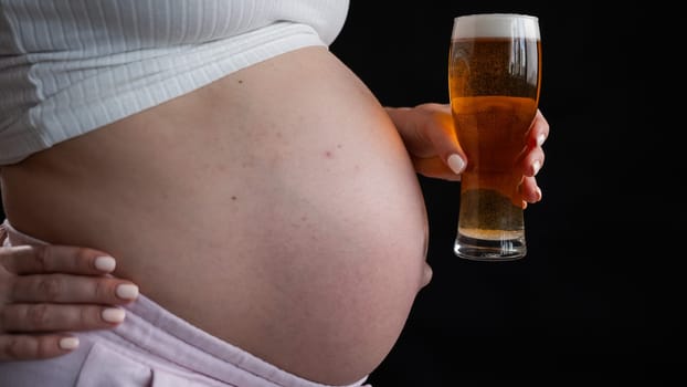 Close-up of the belly of a pregnant woman holding a glass of beer on a black background. Skin rash