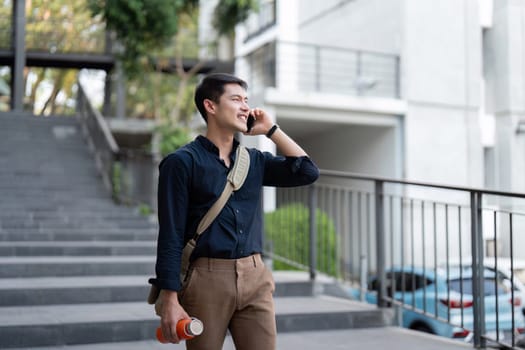 Businessman walking outdoors with a reusable eco-friendly cup, talking on the phone, promoting sustainable lifestyle and eco-friendly practices in an urban environment.