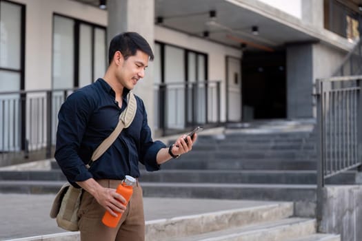 Businessman walking with a reusable eco-friendly cup, checking his phone, promoting sustainable and eco-conscious lifestyle in a modern urban setting.