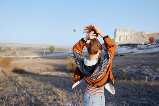 Vibrant redhaired woman standing in field with colorful hot air balloon in background