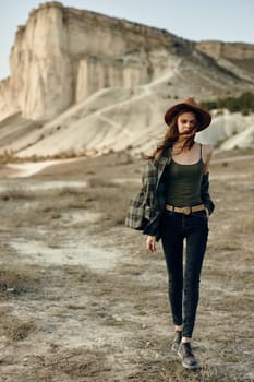 Woman in plaid shirt and hat strolling through sunlit field of wild grass on a summer day