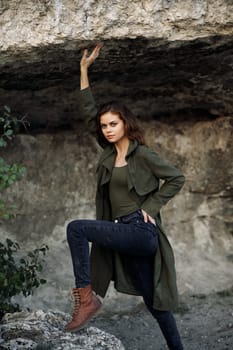 Woman in green coat leaning against rock in serene forest setting