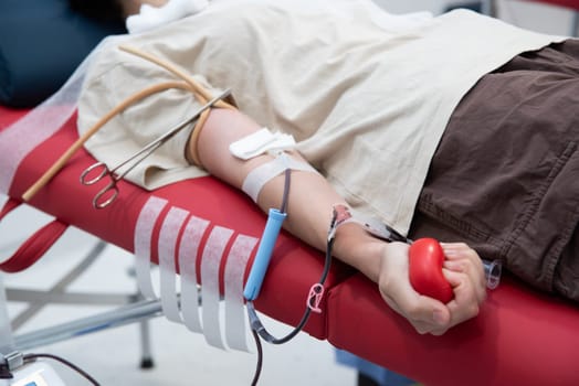 Hand of unrecognizable blood donor squeezing red heart-shaped rubber toy during transfusion process.