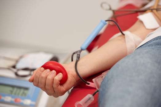 Hand of unrecognizable blood donor squeezing red heart-shaped rubber toy during transfusion process.