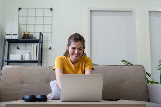 Young woman using a laptop at home, engaging with social media while sitting on a couch in a modern living room.