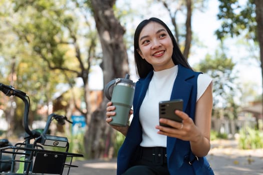 Young professionals enjoy an eco-friendly lifestyle with reusable cups and smartphones in urban parks, promoting sustainable business practices.