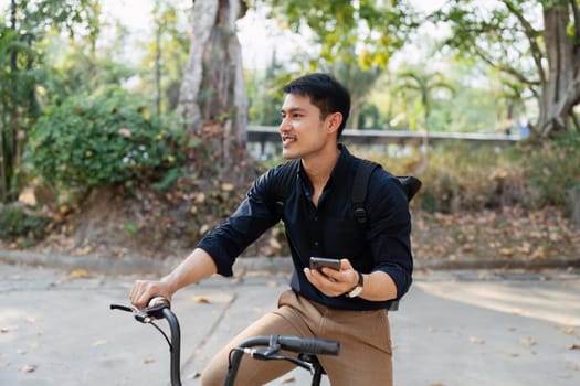 Young man riding a bicycle and using a smartphone outdoors, highlighting an eco-friendly lifestyle with sustainable transportation and digital connectivity.