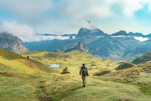 Young man hiking up a grassy hill in the mountains under a cloudy sky, surrounded by lush greenery with a vast landscape spreading in the horizon. High quality photo