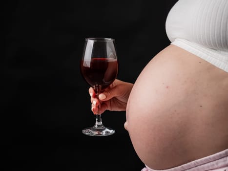 Close-up of the belly of a pregnant woman holding a glass of red wine while sitting on the sofa. Copy space