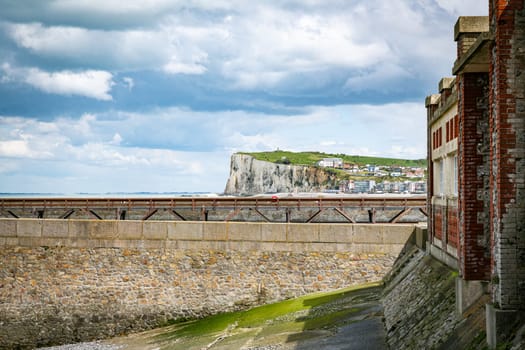 old wooden bridge and lighthouse in the harbor of the french vilage of treport in Normandy with the limestone cliffs of etretat as background