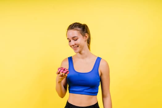 Lovely young caucasian woman in a sports wear with donuts on grey and yellow studio background.